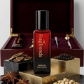 Red perfume bottle with black cap on a decorative stand, surrounded by spices and a wooden box.